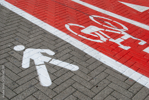 Pedestrian walkway and red bicycle lane with painted traffic symbols on brick pavement, highlighting urban mobility, road safety, sustainable transportation, and shared public space.