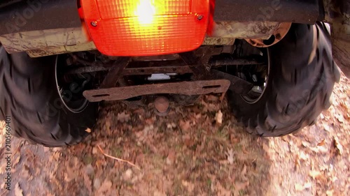 ATV traversing through autumn foliage, showcasing the rugged tires and undercarriage in motion, highlighting the dynamic interaction with the natural terrain and the vibrant environment