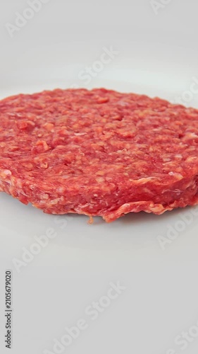 A round piece of raw ground beef is on a plate. vertical video
