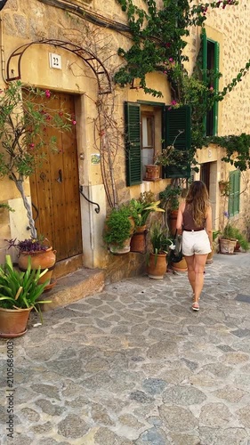 happy woman tourist walking through beauty old town. back view silhouette girl explores enjoys ancient architecture cobbled stone streets, historical village houses decorated with flower pots plants 