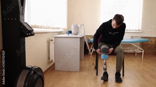 rehabilitation center, adaptation process, prosthetic adjustment. In rehabilitation center, young man sits while fine-tuning his prosthetic leg.