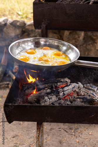 Cooking eggs in a stainless steel pan over an open fire outdoors