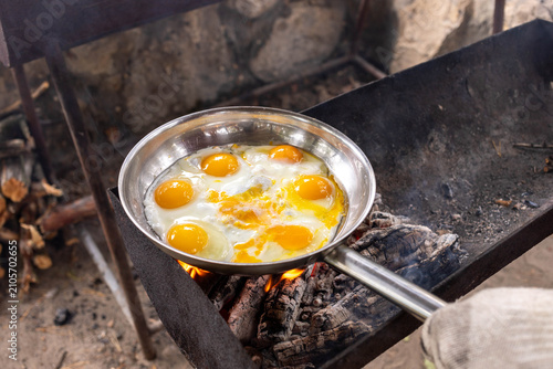 View to cooking eggs in a stainless steel pan over an open fire outdoors