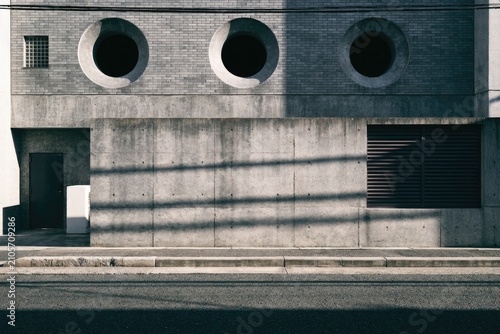 Stark concrete building facade with circular windows, shadows, and street