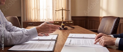 Legal meeting with documents and scales of justice in a formal office setting with individuals formal attire law practice environment depicts two individuals