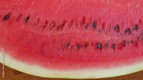 Close up slider shot moving along the slice line of a ripe red watermelon on a wooden table. Cinematic macro footage for summer beverage commercial, organic food and refreshing fruit video concept.