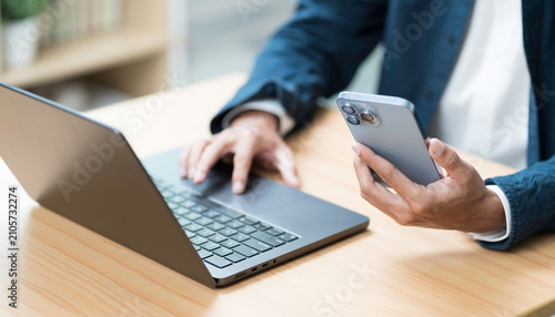 Hands of business man holding mobile phone during using laptop computer on table
