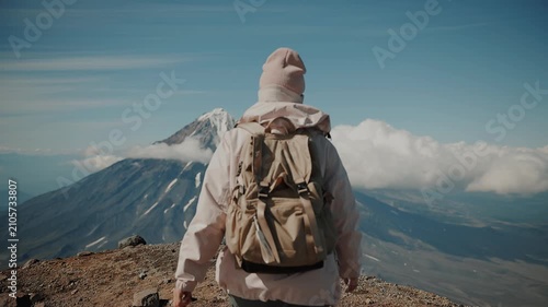 Young girl wearing knitted hat and buff on face climbs to top of ridge and stands against backdrop of snow-capped volcano. Camera changes focus from blurry
