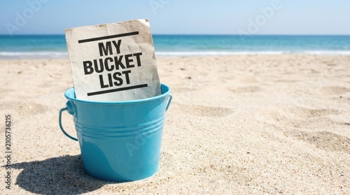 My Bucket List written on paper in a blue bucket on a sandy beach with ocean background.