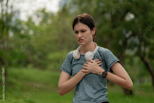 Fotografie Young woman holding chest in pain during outdoor workout, wearing headphones and smartwatch, health emergency, heart problem, fitness risk and active lifestyle, chest, pain, heart, health, emergency