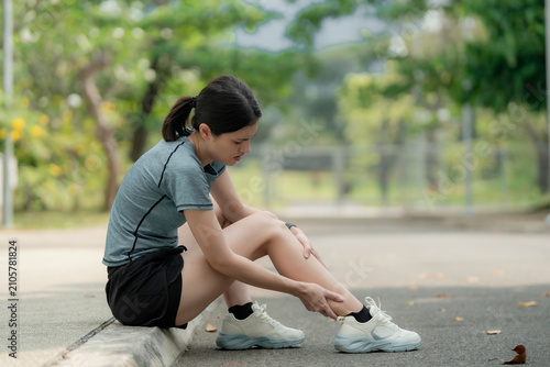 Foto Young woman sitting on curb with leg pain after running in park, holding sore shin muscle, sports injury and overuse strain outdoor fitness concept
