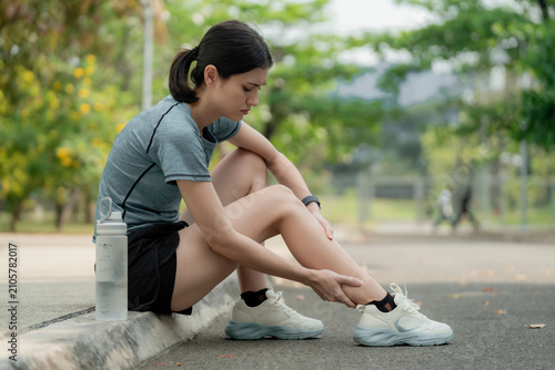 Cuadro en lienzo Young woman sitting on curb with leg pain after running in park, holding sore shin muscle, sports injury and overuse strain outdoor fitness concept