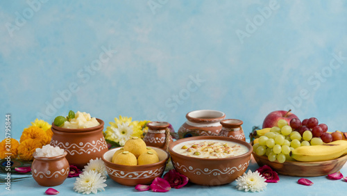 Janmashtami food setup with makhan mishri  peda  kheer  fruits and small clay pots arranged with flowers  soft blue background