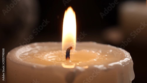 Burning white candle in dark room. Close up of flickering flame for peaceful atmosphere.