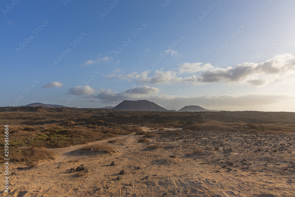 Fototapeta premium Desolate volcanic desert landscape with dirt path leading toward distant mountain cones
