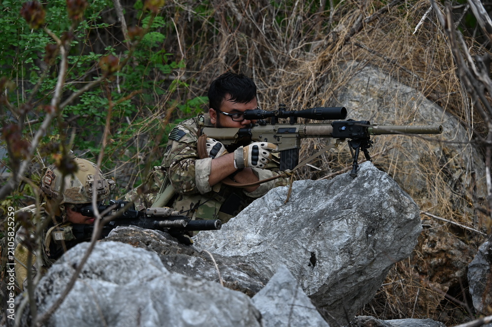 Fototapeta premium Military team in camouflage takes dispersed ambush positions in rocky terrain during a tactical field exercise. Concept of combat simulation, teamwork, defense, and military operations.