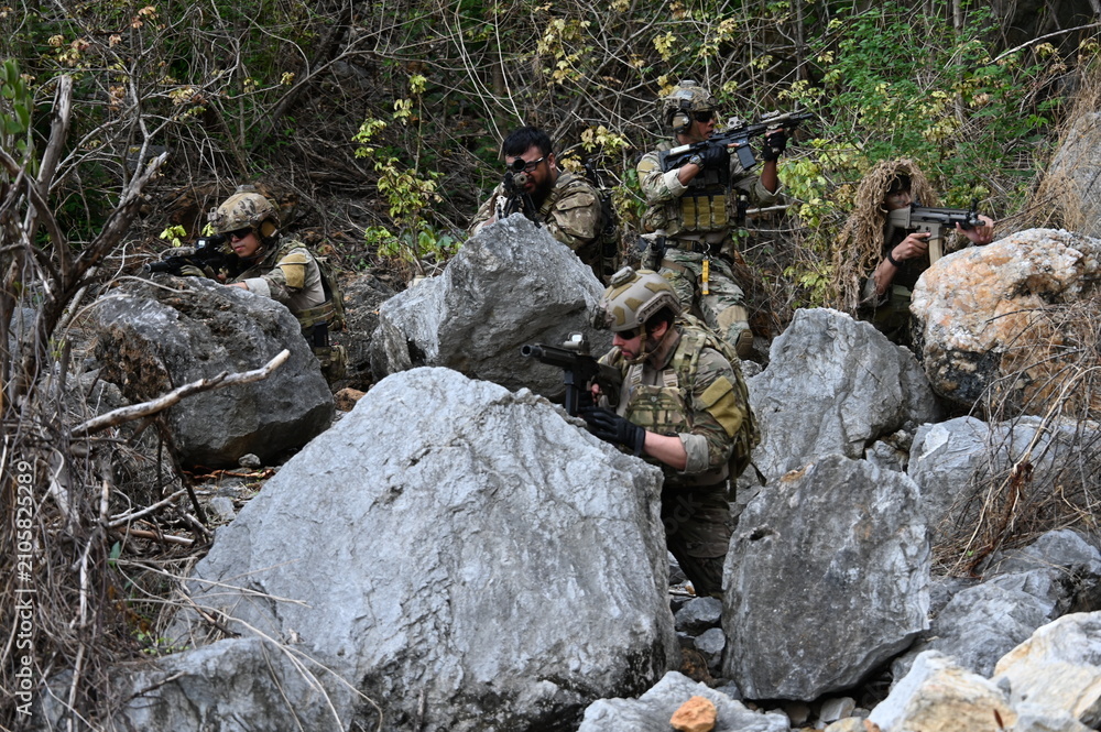Obraz premium Dedicated squad of professional armed military soldiers walking in patrol formation along a rugged rocky mountain cliff during a dangerous tactical combat mission or outdoor training exercise.