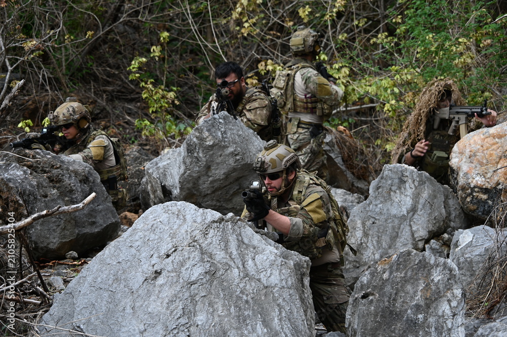 Obraz premium Dedicated squad of professional armed military soldiers walking in patrol formation along a rugged rocky mountain cliff during a dangerous tactical combat mission or outdoor training exercise.