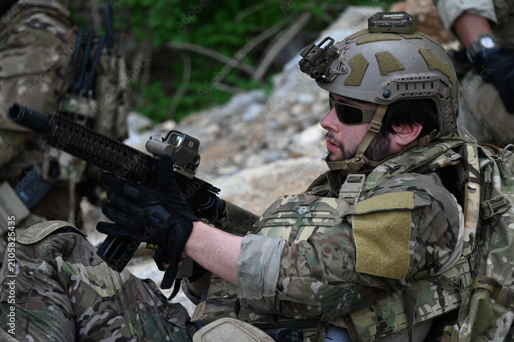 Obraz premium Focused military infantry soldier lying prone on rugged rocky terrain aiming a tactical assault rifle during a dangerous combat training mission for national defense and special security.