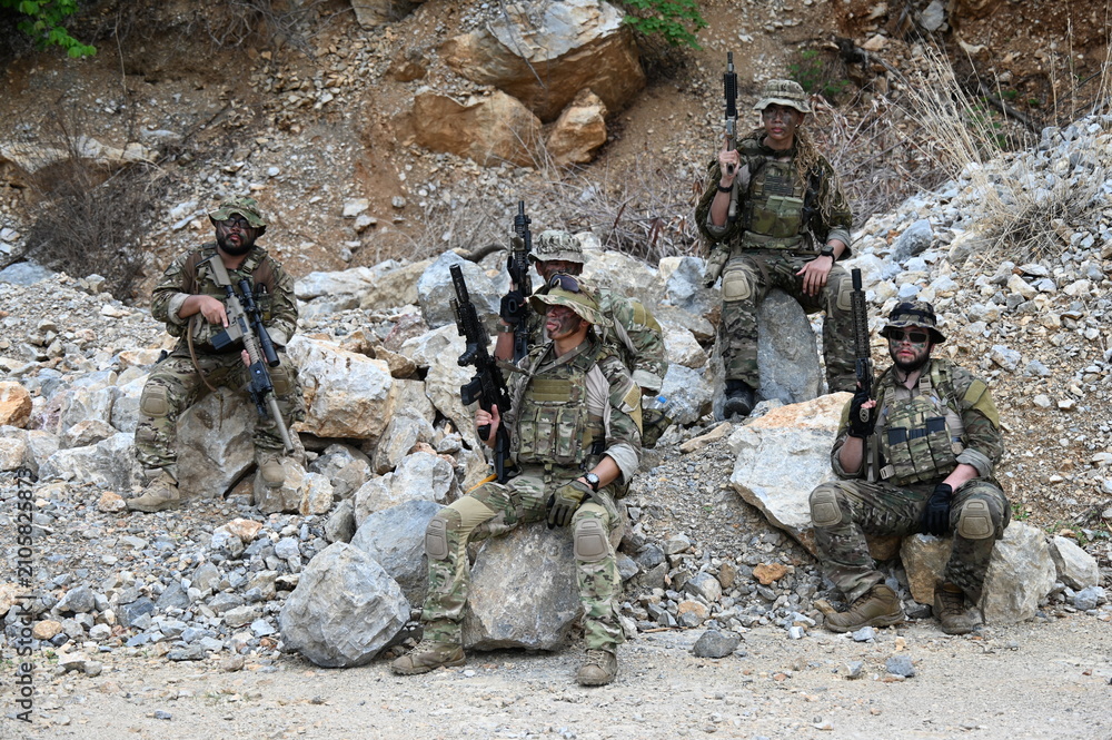 Obraz premium Dedicated squad of professional armed military soldiers walking in patrol formation along a rugged rocky mountain cliff during a dangerous tactical combat mission or outdoor training exercise.
