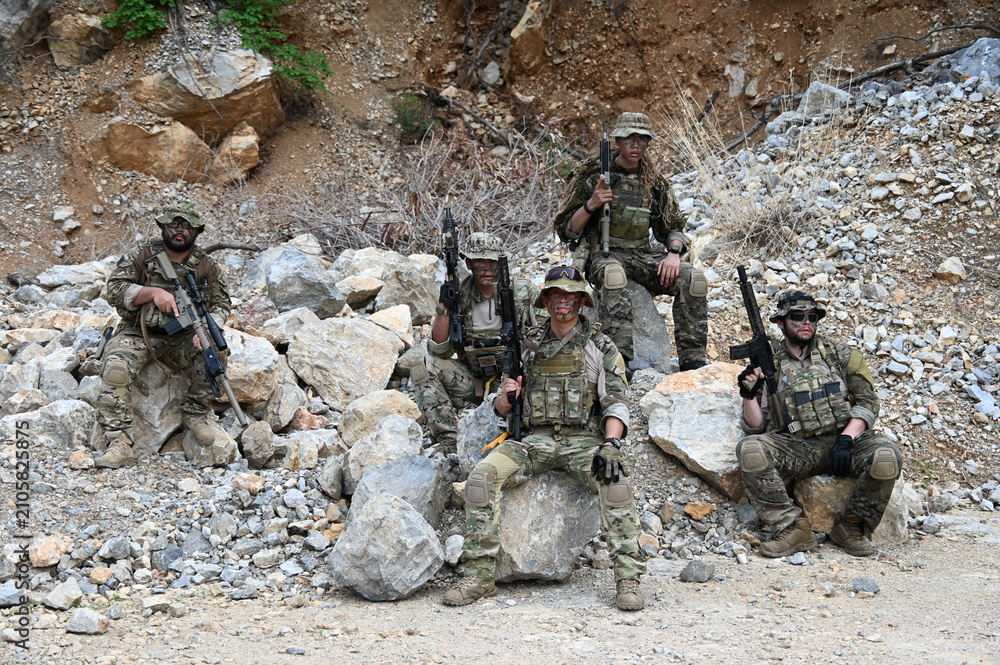 Obraz premium Dedicated squad of professional armed military soldiers walking in patrol formation along a rugged rocky mountain cliff during a dangerous tactical combat mission or outdoor training exercise.