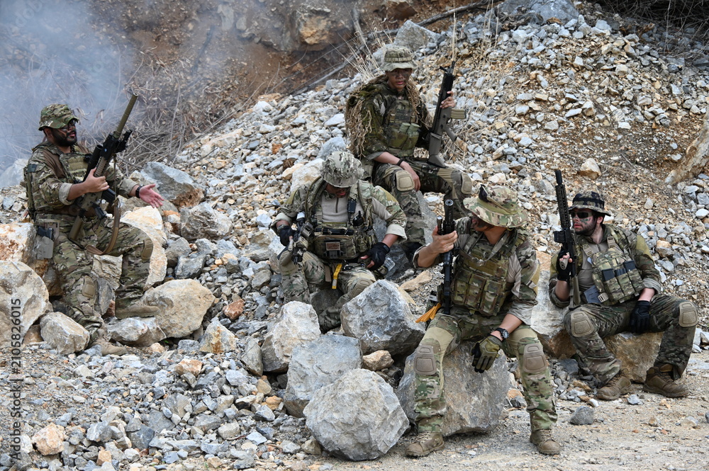 Obraz premium Dedicated squad of professional armed military soldiers walking in patrol formation along a rugged rocky mountain cliff during a dangerous tactical combat mission or outdoor training exercise.