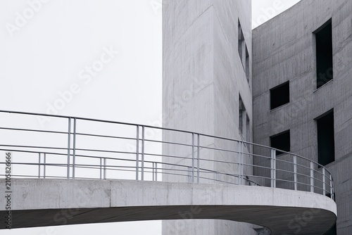Curved concrete walkway with railings leads to modern, angular building