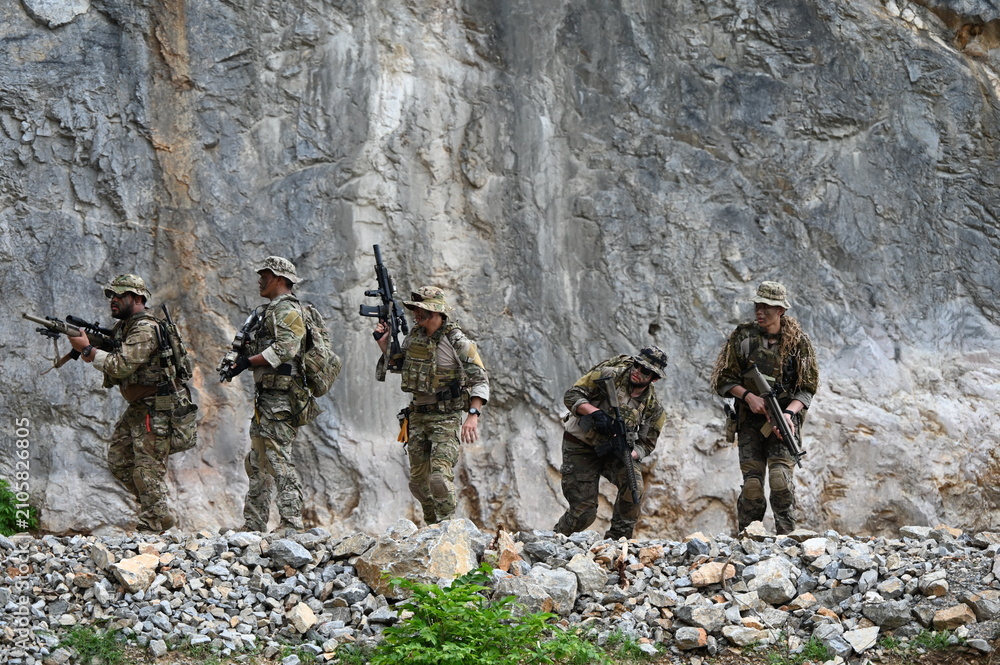 Obraz premium Dedicated squad of professional armed military soldiers walking in patrol formation along a rugged rocky mountain cliff during a dangerous tactical combat mission or outdoor training exercise.