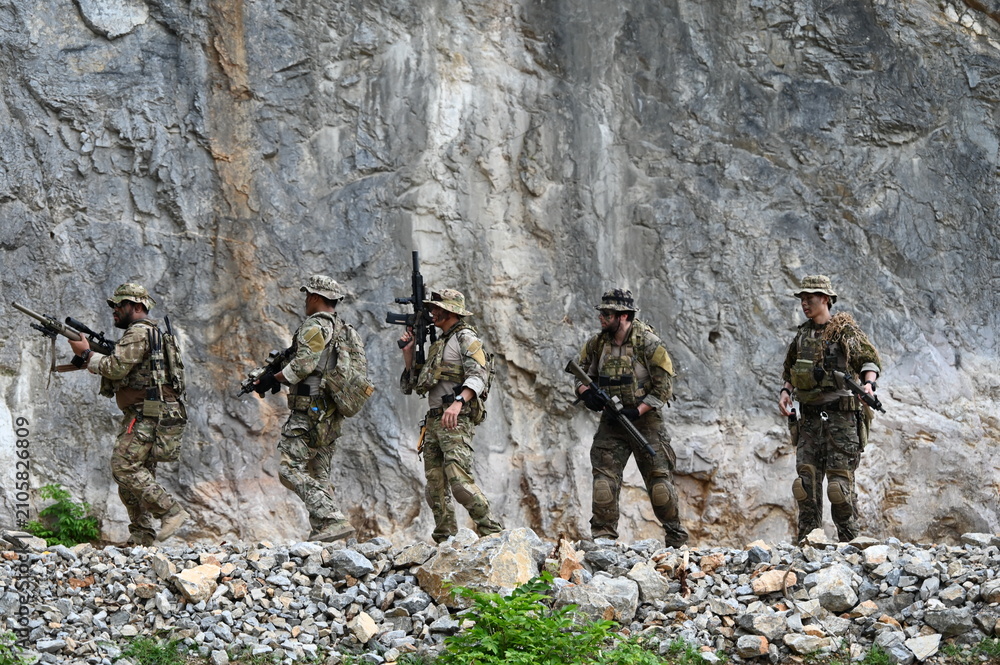 Obraz premium Dedicated squad of professional armed military soldiers walking in patrol formation along a rugged rocky mountain cliff during a dangerous tactical combat mission or outdoor training exercise.