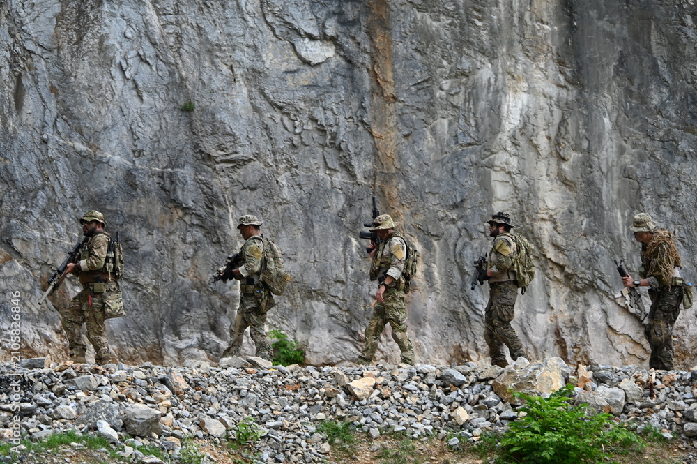 Obraz premium Dedicated squad of professional armed military soldiers walking in patrol formation along a rugged rocky mountain cliff during a dangerous tactical combat mission or outdoor training exercise.