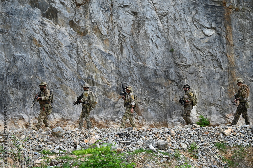 Obraz premium Dedicated squad of professional armed military soldiers walking in patrol formation along a rugged rocky mountain cliff during a dangerous tactical combat mission or outdoor training exercise.