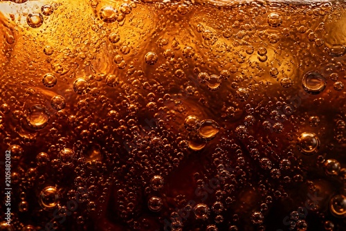 Carbonated beverage bubbles rising in amber liquid closeup