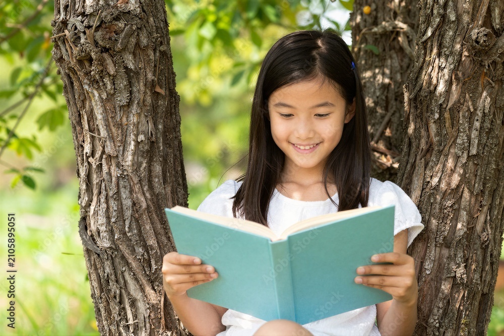 Fototapeta premium Young girl reading book while sitting between tree trunks