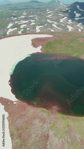 Vertical Drone Shot of Volcanic Crater Lake surrounded by Red Soil, Green Slopes, and Melting Snow
