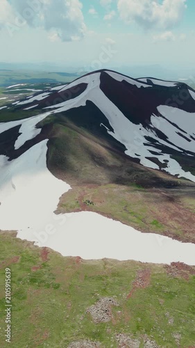 Vertical Drone Shot of Volcanic Crater Lake surrounded by Red Soil, Green Slopes, and Melting Snow