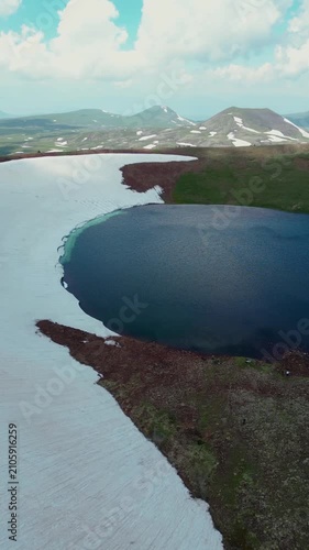 Vertical Drone Shot of Volcanic Crater Lake surrounded by Red Soil, Green Slopes, and Melting Snow