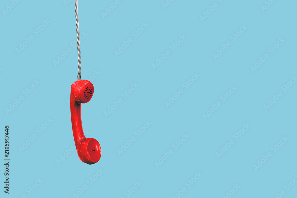 Fototapeta premium A red landline phone hangs by its cord; space available for text, isolated against a neutral background.