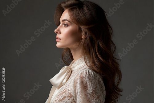 Young woman posing in lace blouse against neutral backdrop