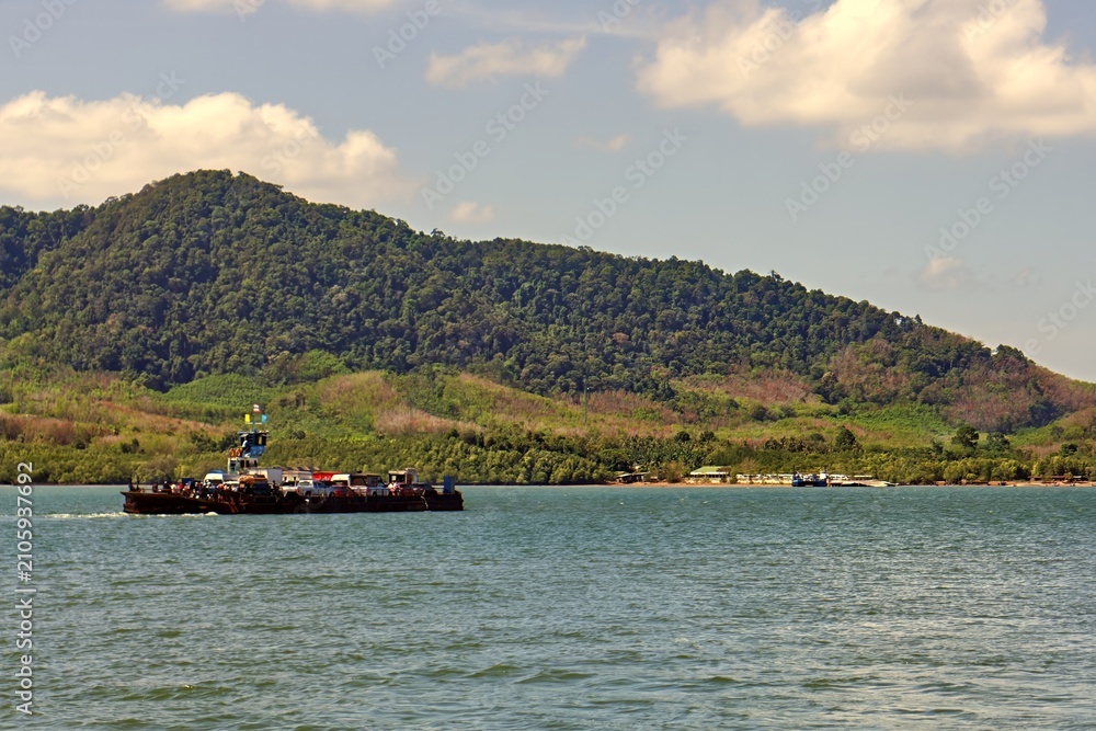 Fototapeta premium Modern passenger transport vessel navigating open ocean waters in Southeast Asia. Coastal scenery of Krabi province visible in the background with visible water wake. 