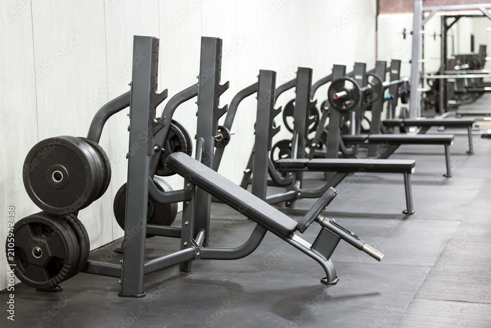 Fototapeta premium Row of bench press stations with plates in gym