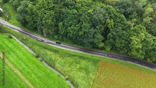 Auto riding through scenic landscape and natural beauty of countryside. Black car driving along winding rural road surrounded by lush greenery. Top view of vehicle trip. Tourism and journey concept