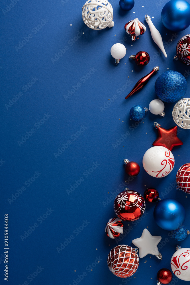 Fototapeta premium Festive red and blue Christmas ornaments and baubles arranged on a navy vertical background for holidays