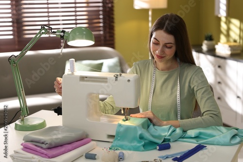 Woman sewing fabric with professional machine at white table in workshop