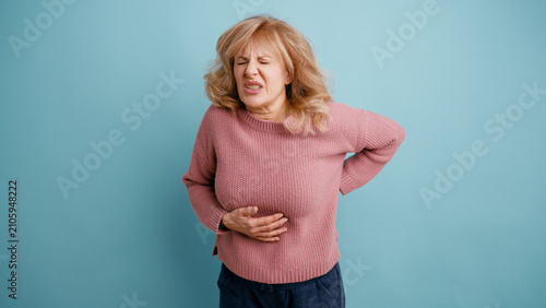 Obraz na plátně Senior woman suffering from severe stomach ache and lower back pain, expressing