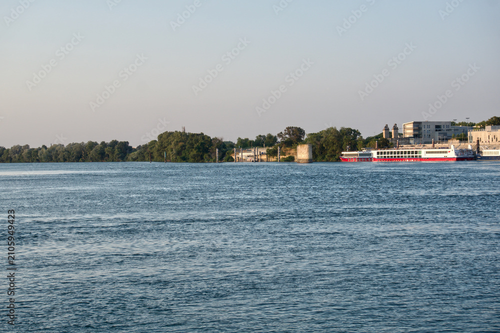 Obraz premium Rhone river flowing past arles coastline with a docked cruise ship at sunset
