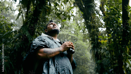 Slika na platnu Hiker in a rainforest exploring nature, looking up with binoculars