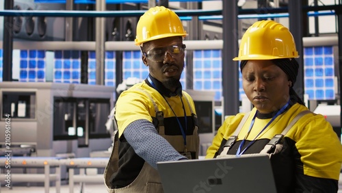 Photography A solar panel plant engineering team uses a laptop to oversee machinery; collaborating colleagues maintain production systems with specialized software