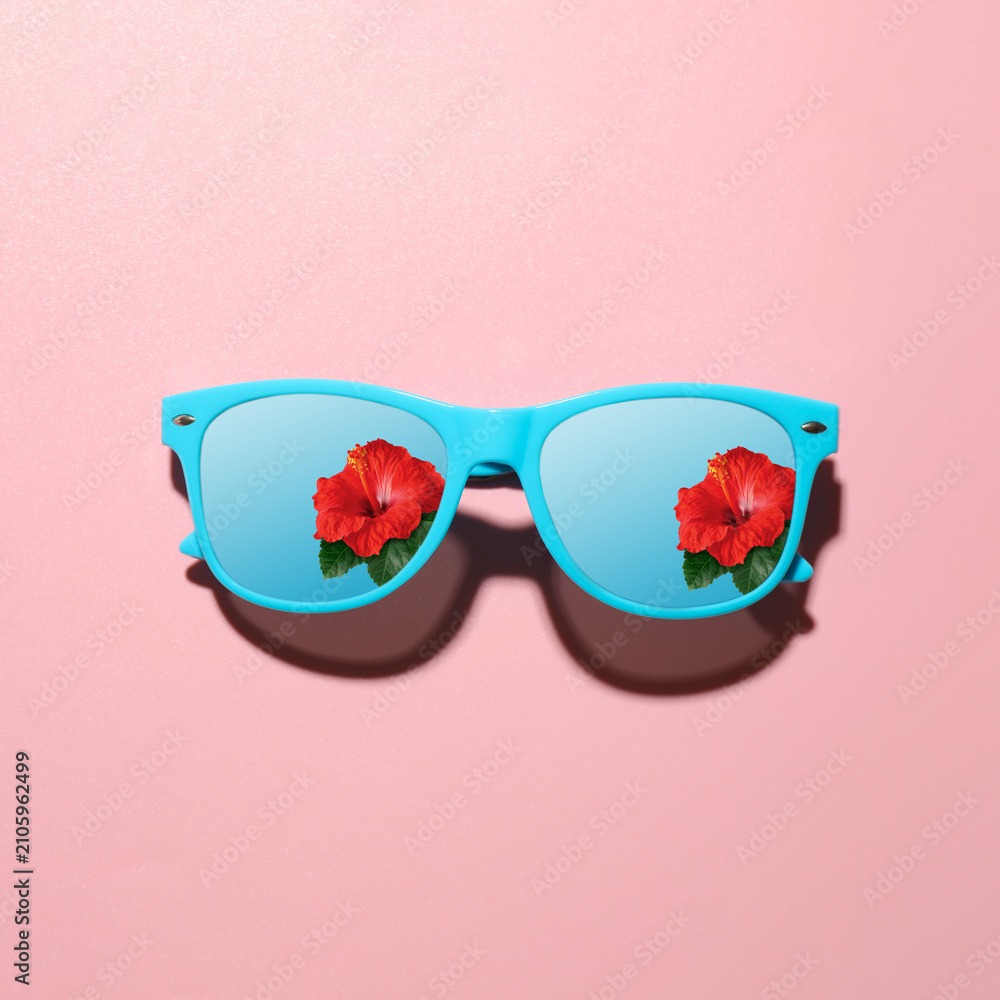Obraz premium Sunglasses with reflection of hibiscus flower under blue sky on pink background