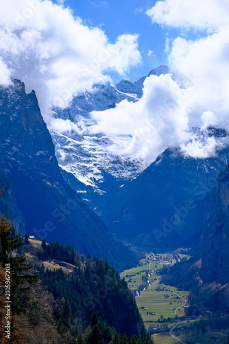 A breathtaking, vertical landscape photograph showcasing the dramatic u-shaped Lauterbrunnen Valley nestled deep between massive limestone cliffs in the Bernese Oberland region. Captured from an eleva
