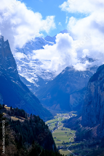 A breathtaking, vertical landscape photograph showcasing the dramatic u-shaped Lauterbrunnen Valley nestled deep between massive limestone cliffs in the Bernese Oberland region. Captured from an eleva